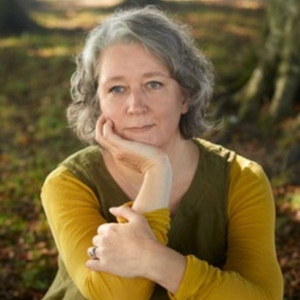Author Claire Fuller, sitting in a forest wearing a yellow top.